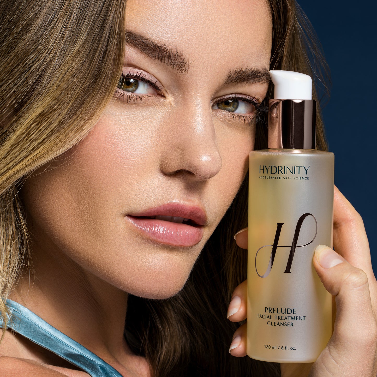 A woman holding the Hydrinity Prelude Cleanser bottle next to her face