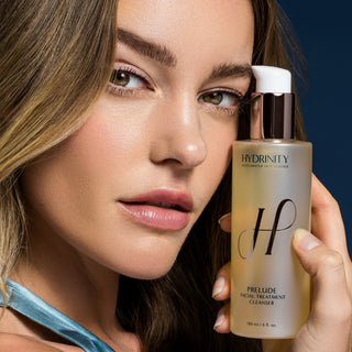 A woman holding the Hydrinity Prelude Cleanser bottle next to her face